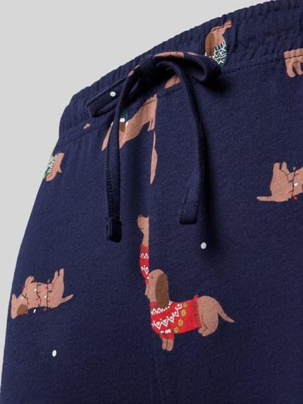 Frauenmodel trägt dunkelblaue Slim Fit Pyjama-Hose aus reiner Baumwolle von Jake*s Casual mit Dackel-Muster, Nahaufnahme Oberkörper.
