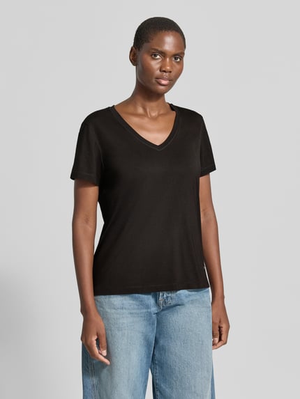 Frauenmodel trägt Regular Fit T-Shirt mit V-Ausschnitt Modell 'Dala' von MOS MOSH, kurzärmelig, schwarz, glatte Textur, Ganzkörperansicht von vorne. Modal-Mix, Label-Emblem, Rückenlänge bei Größe S 58 cm.