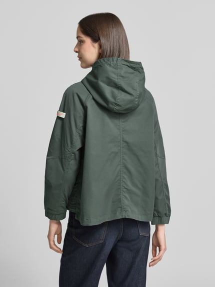 Vrouwenmodel draagt dames jack van katoenmix in recht model, model 'DOLORES NEO' van Frieda & Freddies, kleur groen, labelpatch, capuchon, tweewegritssluiting, knoopsluiting aan klepzakken, elastische mouwboord, verstelbare zoom, ruglengte maat 36: 59 cm, schouderbreedte: 48 cm, borstwijdte: 50 cm, mouwlengte: 52 cm, geheel van achteren.