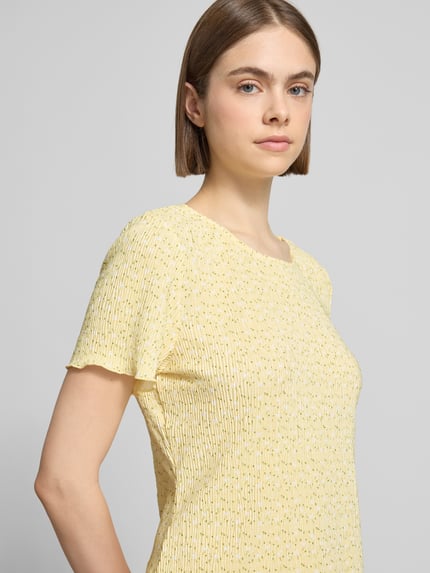 Frauenmodel trägt Slim Fit T-Shirt mit Allover-Muster Modell 'FLORA' von Pieces in Gelb mit Plissee, florales Muster, Nahaufnahme Oberkörper.