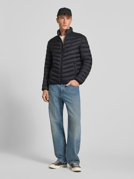 Männermodel trägt Regular Fit Steppjacke mit Logo-Stickerei von REVIEW in Schwarz, Stepp-Optik, Eingrifftaschen, Ganzkörperansicht von vorne.