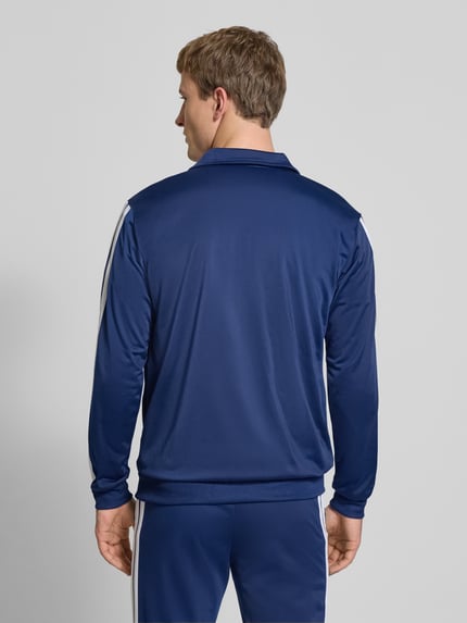 Männermodel trägt blauen Trainingsanzug mit elastischen Abschlüssen von adidas Sportswear, Label-Details, Ganzkörperansicht Rückansicht.