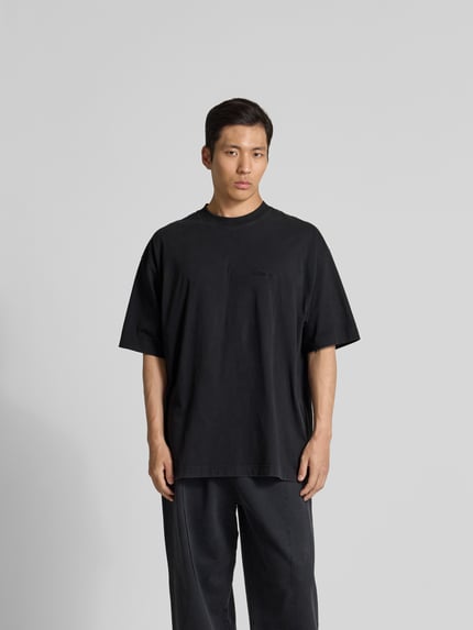 Männermodel trägt Oversized T-Shirt aus Baumwolle von VETEMENTS in Schwarz mit Rundhalsausschnitt, lockerer Schnitt, Ganzkörperansicht von vorne.