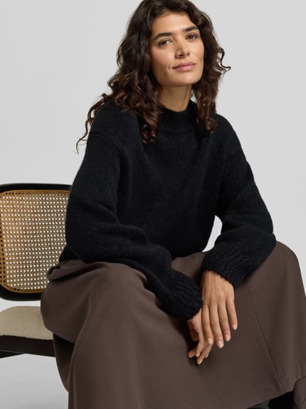 Kobiece model prezentuje sweter aus Wolle Alpaka mit Rippbündchen von MARC CAIN, krój regular fit, imitacja dzianiny, jednokolorowy, krótki krój, opuszczone ramiona, okrągły dekolt, długie rękawy, rękawy i dół wykończone prążkowanymi ściągaczami, Ganzkörperansicht von vorne.