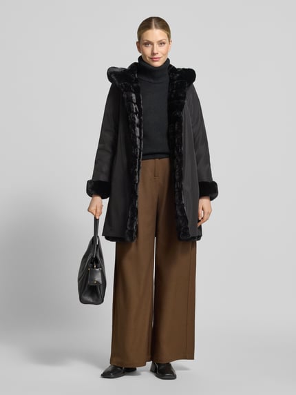 Frauenmodel trägt Regular Fit Mantel mit Wendefunktion und Webpelz-Innenseite von PETITE M., schwarze und braune Töne, Knopfleiste, Eingrifftaschen, mittellanger Schnitt, glatte und flauschige Texturen, Beschreibung laut Kontext, Ganzkörperansicht von vorne.