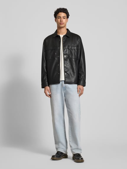Męski model nosi Regular Fit Hemdjacke in Leder-Optik od Calvin Klein Jeans, czarna, długie rękawy, kieszenie na piersi, guzik, krój regular fit, długość tyłu w rozmiarze M: 73 cm, szerokość w rozmiarze M: 50 cm, długość rękawa w rozmiarze M: 65 cm, widok całej sylwetki od przodu.