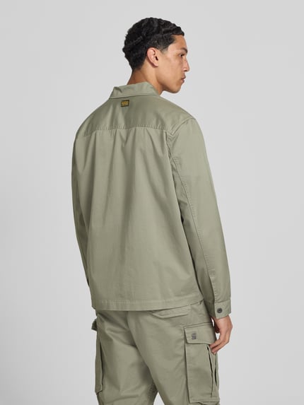 Męski model nosi Hemdjacke mit Kentkragen und Brusttaschen od G-Star Raw w kolorze jasnej oliwki, krój regular fit, listwa guzikowa, kieszenie na piersi, długość tyłu w rozmiarze M: 45 cm, szerokość ramion w rozmiarze M: 61 cm, szerokość klatki piersiowej w rozmiarze M: 58 cm, długość rękawów w rozmiarze M: 67 cm, całkowity widok z tyłu.