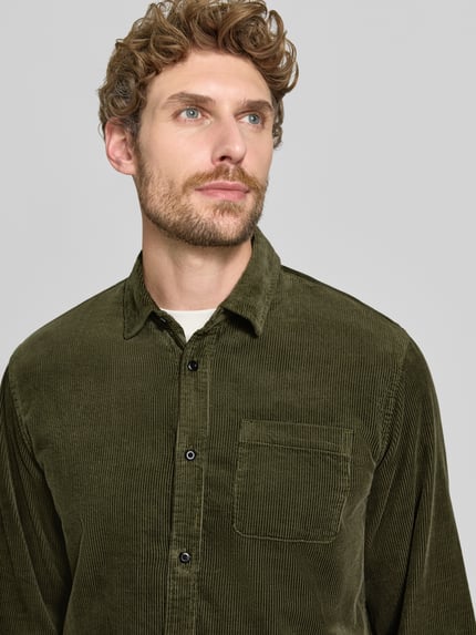 Männermodel trägt Regular Fit Cordhemd mit Brusttasche von Scotch & Soda, grüne Baumwolle mit Kentkragen, Nahaufnahme Oberkörper.