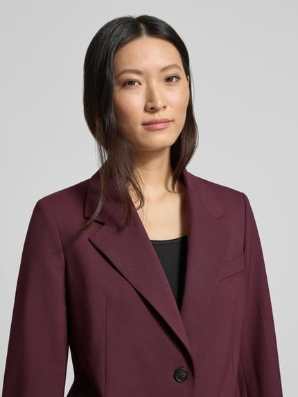 Modelka kobieca ma na sobie Relaxed Fit Kurzblazer aus Wollmix od Tommy Hilfiger, gładki bordowy kolor, 2-guzikowe zapięcie, krój relaxed fit, zbliżenie na górną część ciała od przodu.