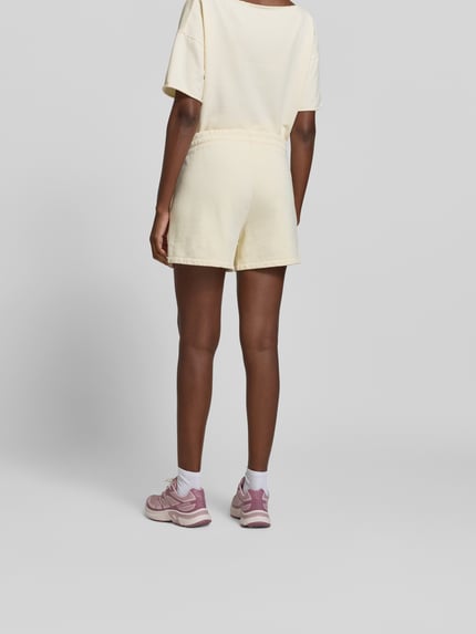 Frauenmodel trägt Shorts mit Modal-Anteil von Juvia in Creme, Baumwoll-Mix, Eingrifftaschen, elastischer Bund, Regular-Fit, Ganzkörperansicht Rückansicht.