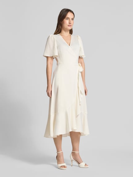 Vrouwenmodel draagt Regular Fit Midikleid in Wickel-Optik Modell 'Thea' van YAS, elastische materiaalmix, kort mouw ontwerp, ruches, licht crèmekleurig, vooraanzicht volledige lengte.