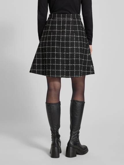 Männermodel trägt Ausgestellter Mini-Rock mit Viskose-Anteil Modell 'RIKLA-1' von HUGO, czarna spódnica w kratę, tkanina bouclé, długość mini, widok całej sylwetki z tyłu.