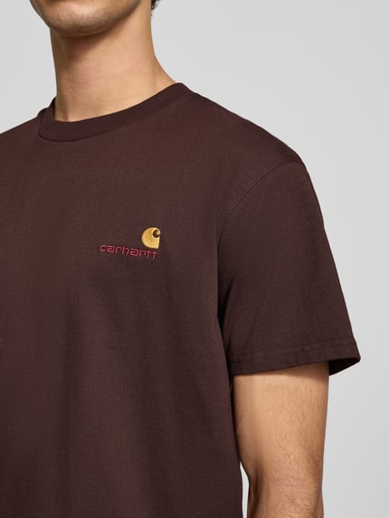 Männermodel trägt T-Shirt mit Label-Stitching von Carhartt Work In Progress in Braun, reine Baumwolle, Regular-Fit, Nahaufnahme Oberkörper.
