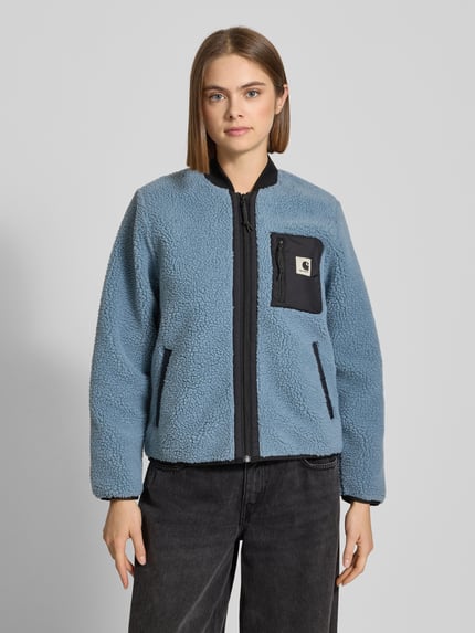 Frauenmodel trägt Fleecejacke im Allover-Look mit Reißverschluss Modell 'Janet' von Carhartt Work In Progress in Blau mit schwarzer Brusttasche, Regular Fit, Nahaufnahme Oberkörper.