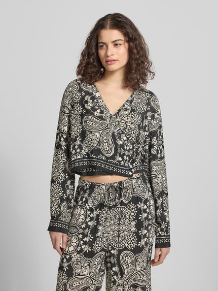 Frauenmodel trägt Shaped Fit Bluse aus reiner Viskose Modell 'LEMZA' von Only mit florales-Allover-Muster, Wickeloptik, Bindegürtel, V-Ausschnitt, Langarm, Manschette, feine Webstruktur, Farbe Schwarz-Creme, Ganzkörperansicht von vorne.