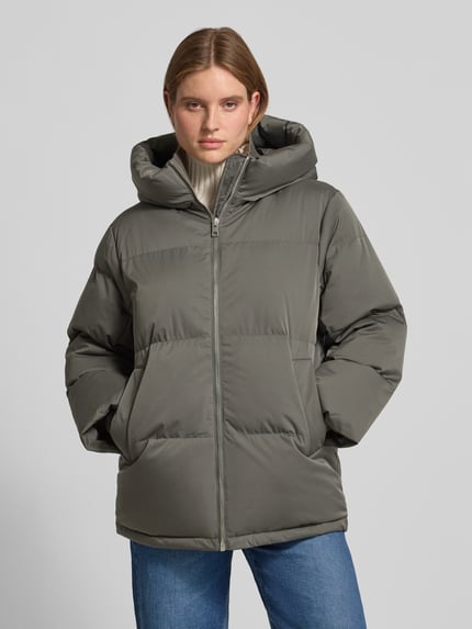 Vrouwenmodel draagt Loose fit pufferjack met capuchon Model 'Hilena' van OPUS, look: effen, lang, ritssluiting, lange mouw, steekzakken, waterafstotend, winddicht, geribde stormcuffs, recht rompzoom, materiaalverwerking: gewatteerd, vooraanzicht van het hele lichaam.