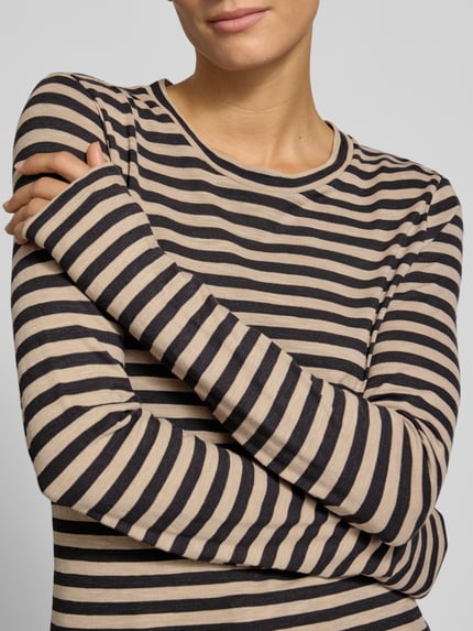 Frauenmodel trägt Langarmshirt mit Rollsaum-Details von MARC O'POLO im gestreiften Allover-Muster, Jersey-Longline, Nahaufnahme Oberkörper.