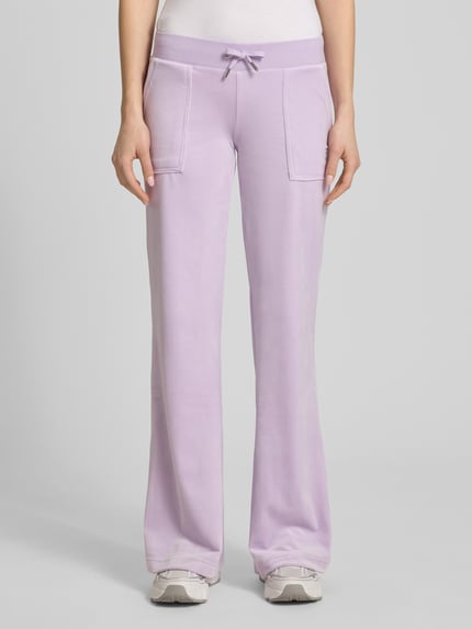 Frauenmodel trägt Low Rise Sweatpants mit Eingrifftaschen Modell 'LAYLA' von Juicy Couture, Lila, Material-Mix mit Stretch-Anteil, elastischer Bund, Ganzkörperansicht von vorne, Damen, Innenbeinlänge bei Größe S 82 cm.