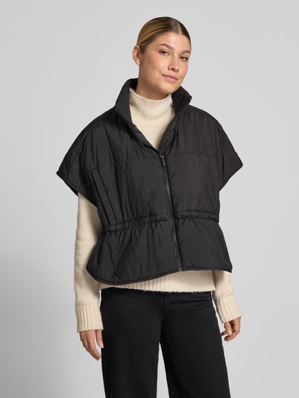 Frauenmodel trägt Steppweste mit Stehkragen Modell 'Vanjah' von someday, relaxed Fit, schwarzer Stoff, sichtbarer Reißverschluss, Ganzkörperansicht von vorne. Rückenlänge 58 cm, Schulterbreite 75 cm, Brustweite 59 cm.