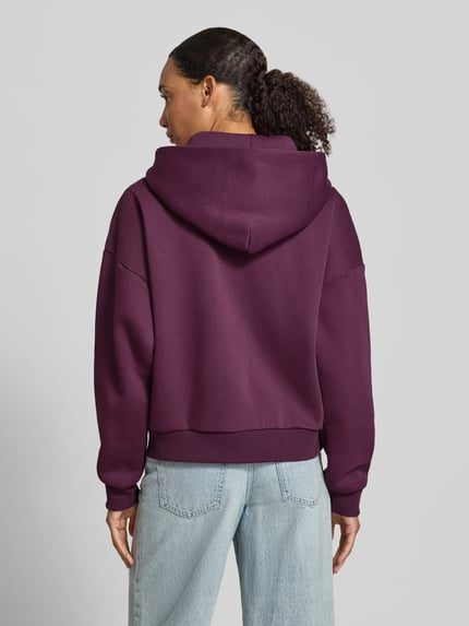 Vrouwenmodel draagt Relaxed Fit Sweatjacke aus Baumwoll-Mix mit Label-Detail van REVIEW, paarse kleur, katoenmix, met capuchon, kangoeroezak en elastische boorden, katoenstructuur, zachte look, volledige rugaanzicht.