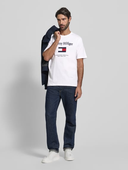 Männermodel trägt Regular Fit T-Shirt aus reiner Baumwolle von Tommy Hilfiger, unifarben, Rundhals, kurzarm, Label-Schriftzug, Ganzkörperansicht von vorne.