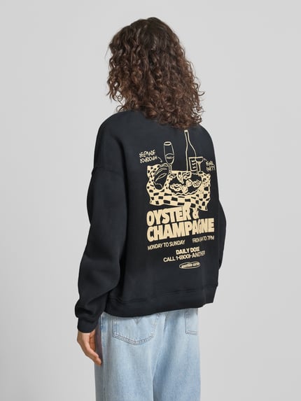 Modelka nosi Regular Fit Sweatshirt mit Logo-Print od ANOTHER COTTON LAB, mieszanka bawełny, stójka, elastyczne wykończenia, nadruk z logo, widok całej sylwetki z tyłu.