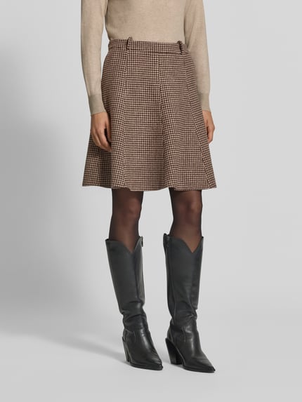 Frauenmodel trägt Ausgestellter Mini-Rock aus reiner Wolle von GANT, braunes Hahnentritt-Muster, kombiniert mit Stiefeln, Nahaufnahme Oberkörper.