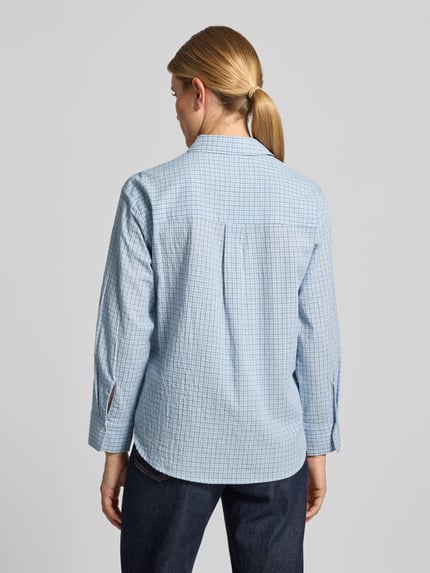 Frauenmodel trägt Relaxed Fit Hemdbluse aus reiner Baumwolle Modell 'CHUACKUA' von MANGO in hellblau kariert, verlängerte Rückseite, Ganzkörperansicht Rückansicht.