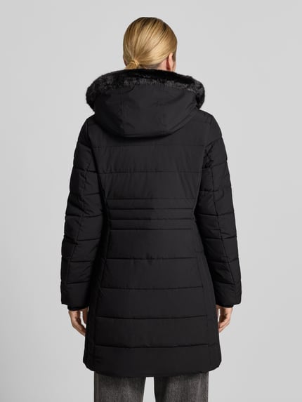 Frauenmodel trägt Jacke mit abnehmbarer Kapuze Modell 'ECLIPSE' von NAUTGÅRD in Schwarz, gesteppte Struktur, Ganzkörperansicht Rückansicht, gerader Schnitt, seitliche Eingrifftaschen und gestrickte Ärmelabschlüsse, Kontext: Zweiwege-Reißverschluss, Label-Patch, Rückenlänge 79 cm, Schulterbreite 38 cm, Brustweite 48 cm, Ärmellänge 62 cm