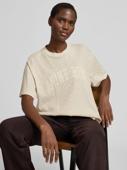 Kobiece model prezentuje damski t-shirt z bawełny, krój oversized fit, nadruk z logo, zwierzęcy nadruk na całej powierzchni, okrągły dekolt, długość tyłu w rozmiarze s: 64 cm, oversize t-shirt mit logo-print od anine bing, jasne beże, subtelna faktura, gładkie wykończenie. Zbliżenie na górną część ciała z przodu.