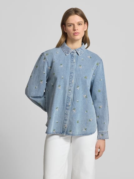 Frauenmodel trägt Relaxed Fit Jeansbluse aus reiner Baumwolle Modell 'VERA' von Only mit florale-Stickereien in Denim-Optik, Hemdblusenkragen, verdeckte Knopfleiste, Rückenpasse, Manschette, abgerundeter Rumpfabschluss, Ganzkörperansicht von vorne.