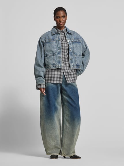 Frauenmodel trägt Oversized Hemdbluse aus reiner Baumwolle von black palms mit durchgehender Knopfleiste, Brusttasche und Hemdblusenkragen, grau kariert, kombiniert mit blauer Jeansjacke und heller Oversized-Jeans, Ganzkörperansicht von vorne, Rückenlänge bei Größe S: 70 cm.