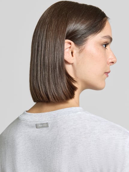 Frauenmodel trägt Relaxed Fit T-Shirt aus Baumwoll-Mix von Fabletics in Hellgrau, glatte Textur, Detailaufnahme Rückenansicht.