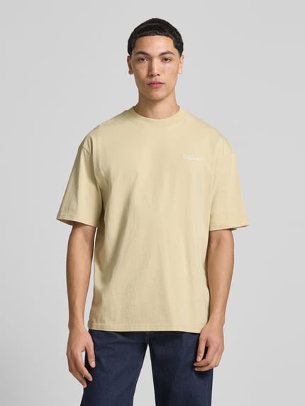 Męski model nosi Oversized Fit T-Shirt mit Logo-Stitching od Pegador z bawełny, krój oversized fit, okrągły dekolt, długość tyłu 71 cm, jasnobeżowy, gładka faktura, Ganzkörperansicht von vorne.