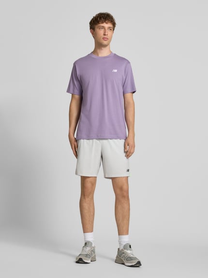 Männermodel trägt T-Shirt mit Logo und Rundhalsausschnitt von New Balance in Lila, Reine Baumwolle, Regular-Fit, Rückenlänge 74 cm, Ganzkörperansicht von vorne