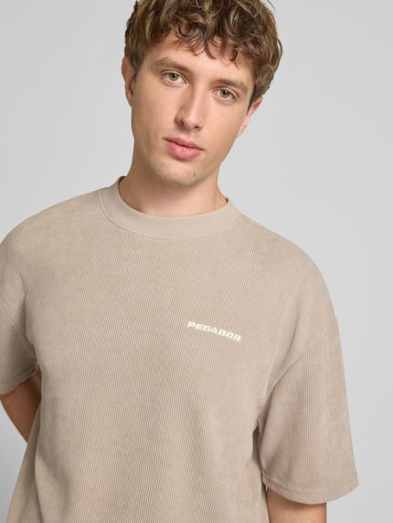 Männermodel trägt Oversized T-Shirt mit Logo-Stitching Modell 'Lagos' von Pegador, Elastischer-Material-Mix, Oversized-Fit, Nahaufnahme Oberkörper.