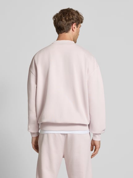 Männermodel trägt Oversized Sweatshirt mit Label-Stitching von Pegador aus Baumwoll-Mix in hellem Rosa, Rückenlänge 70 cm, ganzkörperansicht Rückansicht.