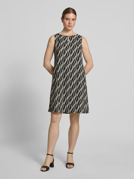 Vrouwenmodel draagt Knielanges Kleid mit Schlüsselloch-Ausschnitt van Betty Barclay, materiaalmix met stretch, straight fit, knielengte, ruglengte maat 36: 91 cm, borstwijdte maat 36: 44 cm, geometrisch patroon in zwart en beige, gladde textuur, geheel vooraanzicht.