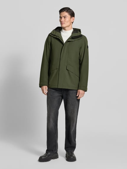 Männermodel trägt Regular Fit Jacke mit Kapuze Modell 'Adam' von Didriksons in Olivgrün, Eingrifftaschen, Ganzkörperansicht von vorne. Rückenlänge 79 cm, Schulterbreite 46 cm, Brustweite 58 cm, Ärmellänge 73 cm.