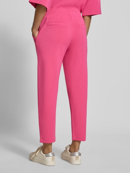 Frauenmodel trägt Sweatpants mit seitlichen Eingrifftaschen von Christian Berg Woman in Pink, lockere Passform, Ganzkörperansicht Rückansicht.
