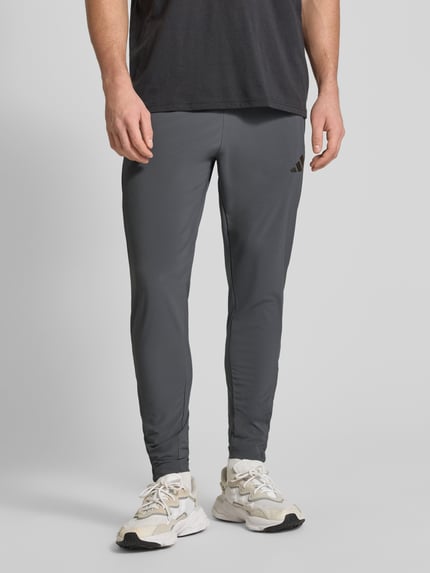 Mężczyzna prezentuje Regular Fit Jogpants mit elastischem Bund Modell 'TIRO' od adidas Sportswear, szary kolor, widok z przodu, zbliżenie na nogi.