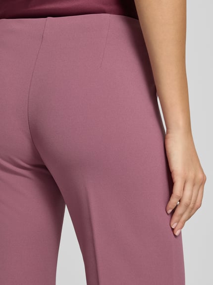 Frauenmodel trägt Flared Fit Stoffhose mit Bügelfalten von Rinascimento in Altrosa, glatte Struktur, elastischer Bund, Detailaufnahme, Damen Stoffhose von Rinascimento, Material-Mic mit Stretch-Anteil, Bundweite S 38 cm, Innenbeinlänge S 85 cm.
