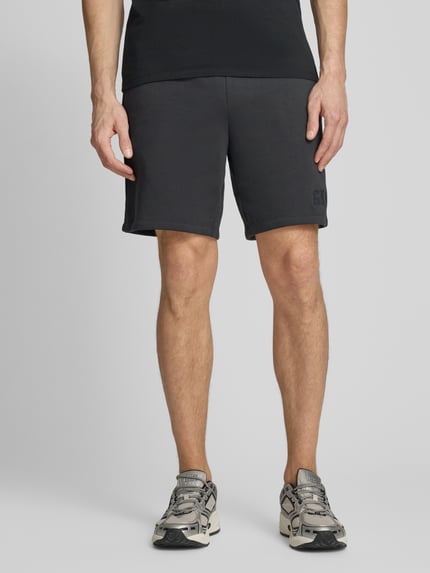 Männermodel trägt Sweatshorts mit elastischem Bund von GAP aus Baumwoll-Mix mit Logo, Relaxed-Fit, Ganzkörperansicht von vorne.