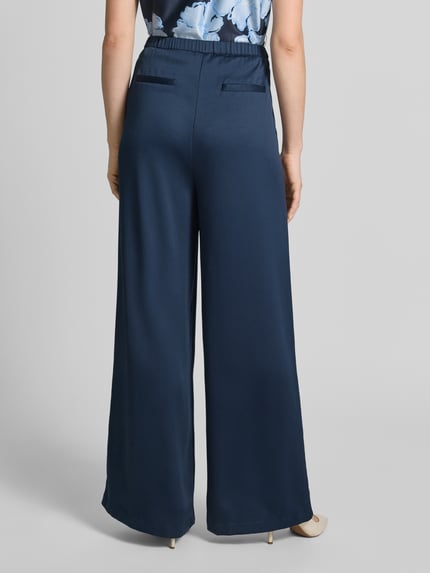 Frauenmodel trägt Loose Fit Pants mit elastischem Bund und Eingrifftaschen von Christian Berg Cocktail in Dunkelblau, Lockerer-Schnitt, Gesäßleistentaschen, Ganzkörperansicht Rückansicht.