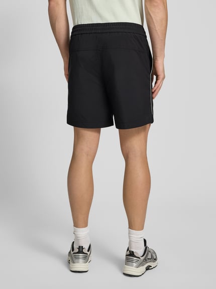 Mężczyzna model nosi Regular Fit Shorts mit Label-Applikation Modell 'COLAS262S' od HUGO, efekt: jednolity kolor, krój regular fit, aplikacja z metką, paski w kontrastowym kolorze, elastyczny ściągacz z tunelem, wpuszczane kieszenie, widok całej sylwetki z tyłu