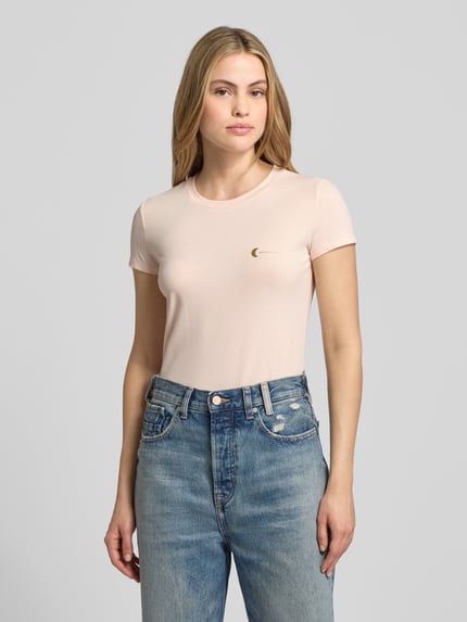 Vrouwenmodel draagt T-Shirt met Label-Print van ARMANI EXCHANGE in lichtroze, slim fit, katoen-elastaan, geribde ronde hals, voorkant volledig zichtbaar, bovenlichaam close-up.