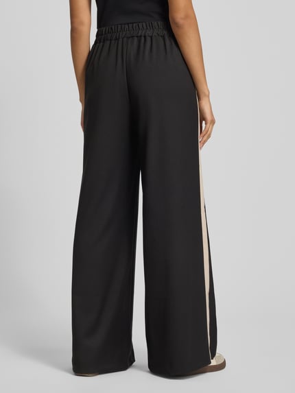 Kobieta modelka nosi Stoffhose mit weitem Bein und elastischem Bund od Rinascimento, czarny materiał, szeroka nogawka, elastyczny pas, tkanina mieszana z dodatkiem wiskozy, kieszenie, detal z logo, widok całej sylwetki z tyłu.
