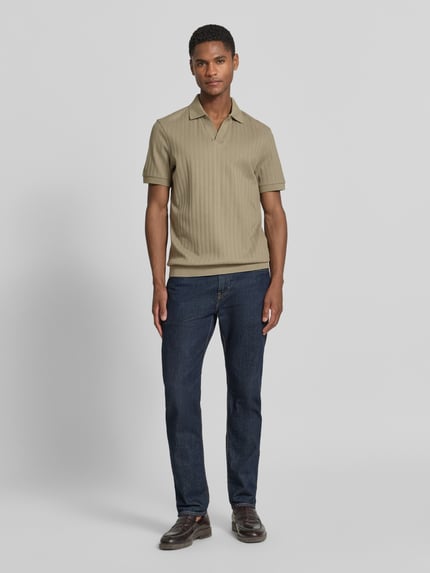 Męski model nosi koszulkę polo Regular Fit Poloshirt mit V-Ausschnitt Modell 'Baronito' von JOOP! Collection z bawełny, fakturowany wzór, dekolt w serek, długość tyłu w rozmiarze M: 69 cm, kolor beżowy, ciemnoniebieskie jeansy, pełny widok z przodu.