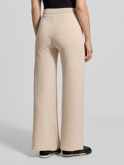Vrouwenmodel draagt Wide Leg Sweatpants met logo-motief model 'LAUDOMIA' van GUESS Activewear in beige met elastische tailleband, materiaal-mix met stretch, detailopname van achteren.