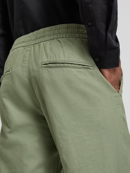 Männermodel trägt Straight Fit Leinenhose mit elastischem Bund Modell 'Barton' van Matinique in lichtgroen, mix van katoen en linnen, met achterzakken, detailaufnahme achterkant.